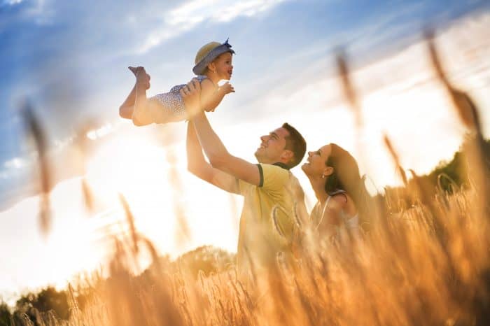 Happy pregnant family with little daughter spending time together in sunny field