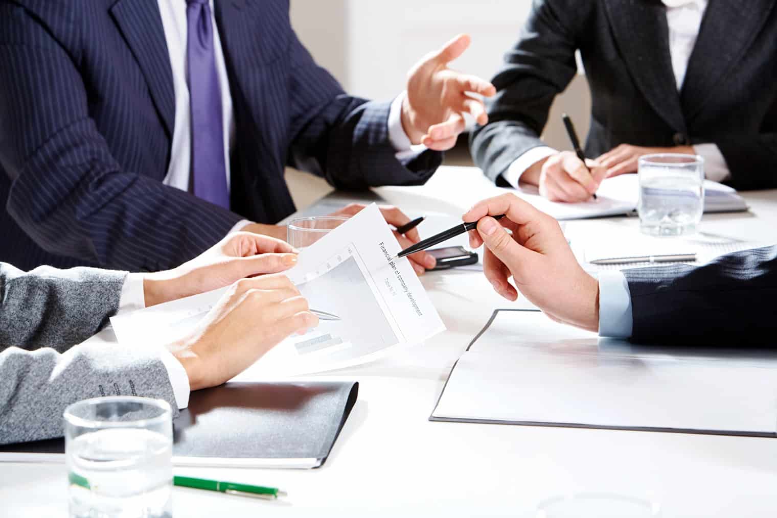 Close-up of businessman hand with pen explaining a financial plan to colleagues at meeting